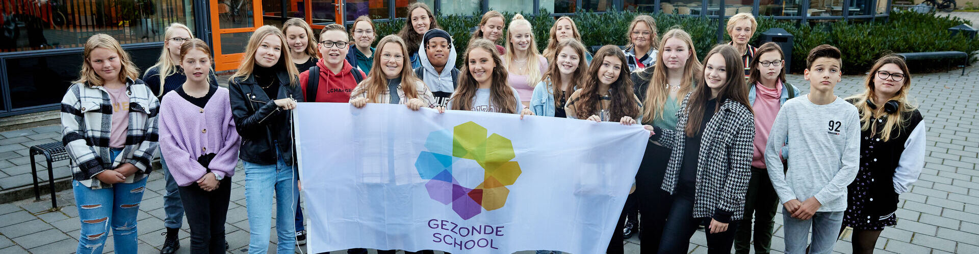 Decoratieve foto: een groep van leerlingen en docent poseert voor de foto, met een vlag van Gezonde School vast