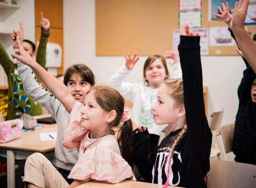 Decoratieve foto van blije leerlingen die hun vinger opsteken in de klas
