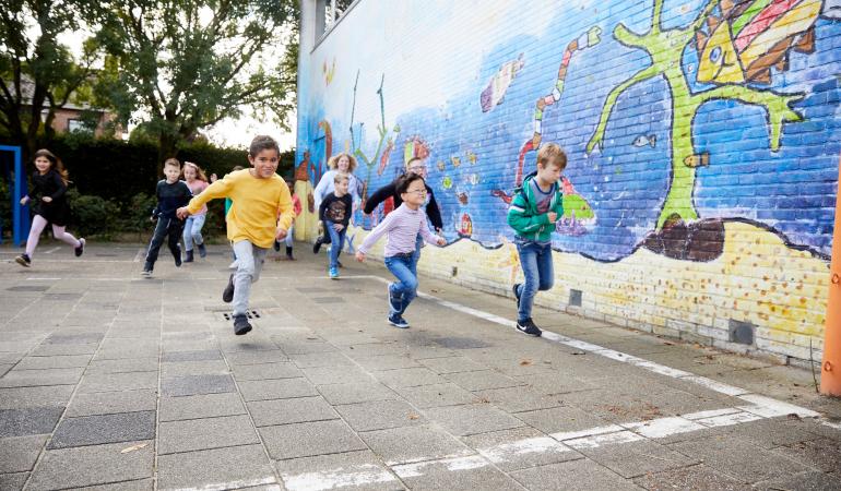 Kinderen rennen buiten op het schoolplein langs een muurschildering