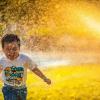 Foto van een jongetje dat lachend door gesproeid water rent